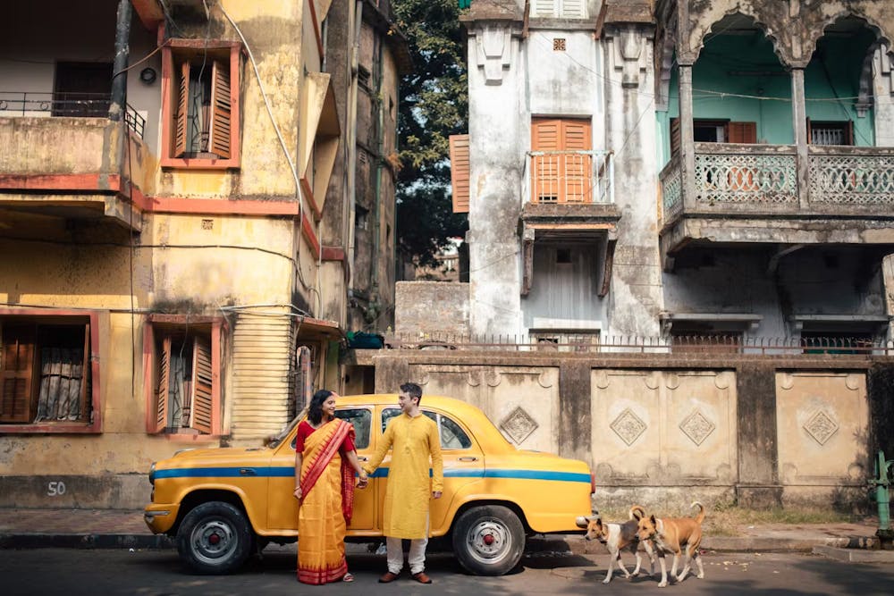 Indian couple in front of yellow taxi in Kolkata for traditional pre wedding photoshoot | Memories Designer