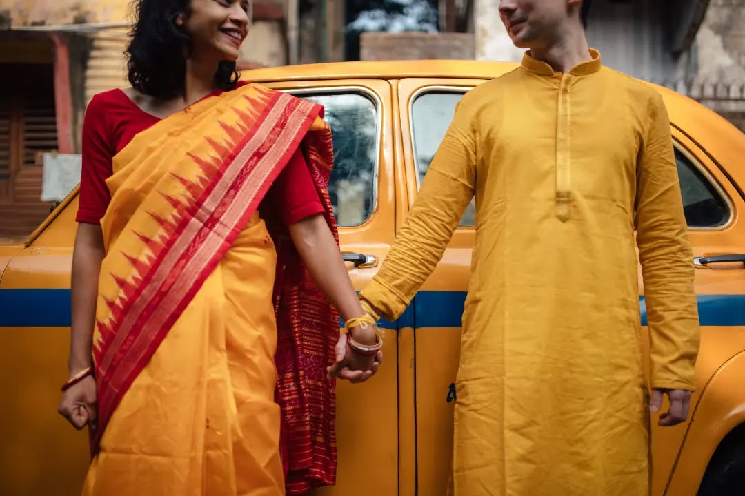 Funny wedding photography ideas where Indian bride and groom are holding hands in front of a yellow taxi in Kolkata | Memories Designer