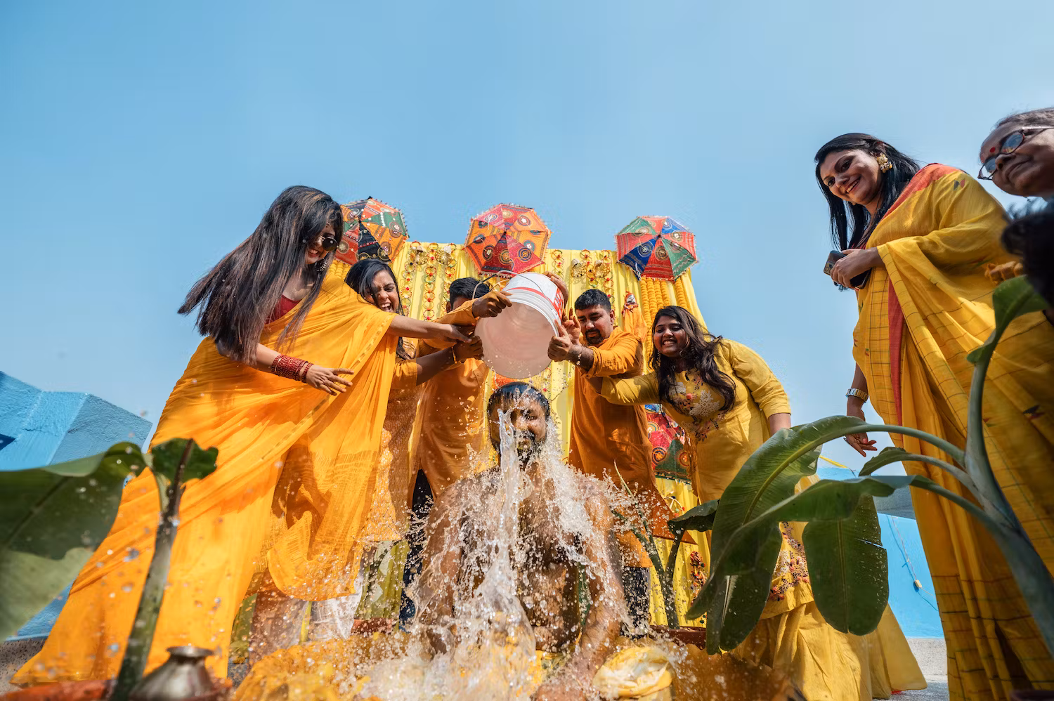 Family and friends of groom bathing him with water after Haldi rituals