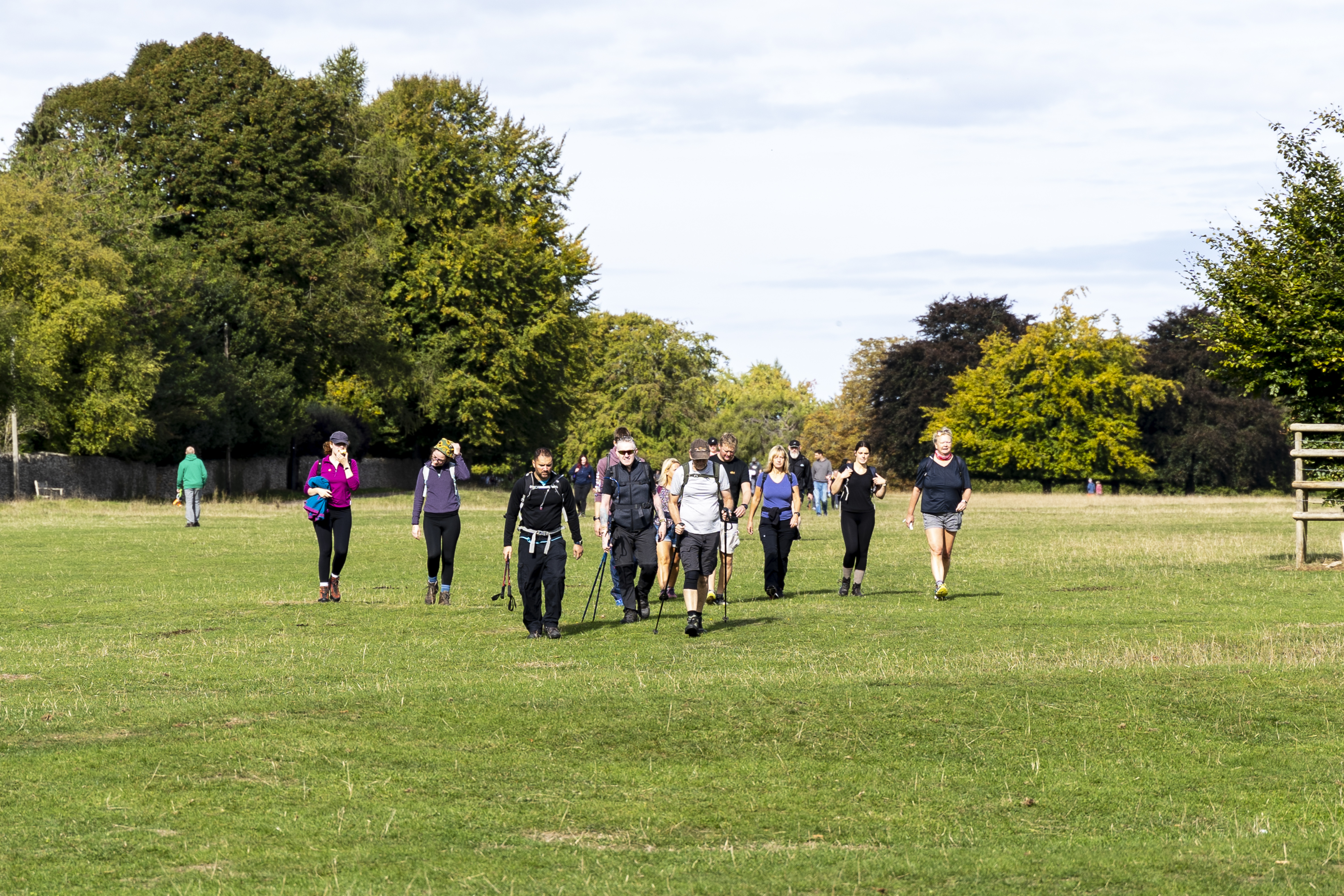 Photo of a group of adults walking through a green field, wearing walking gear.