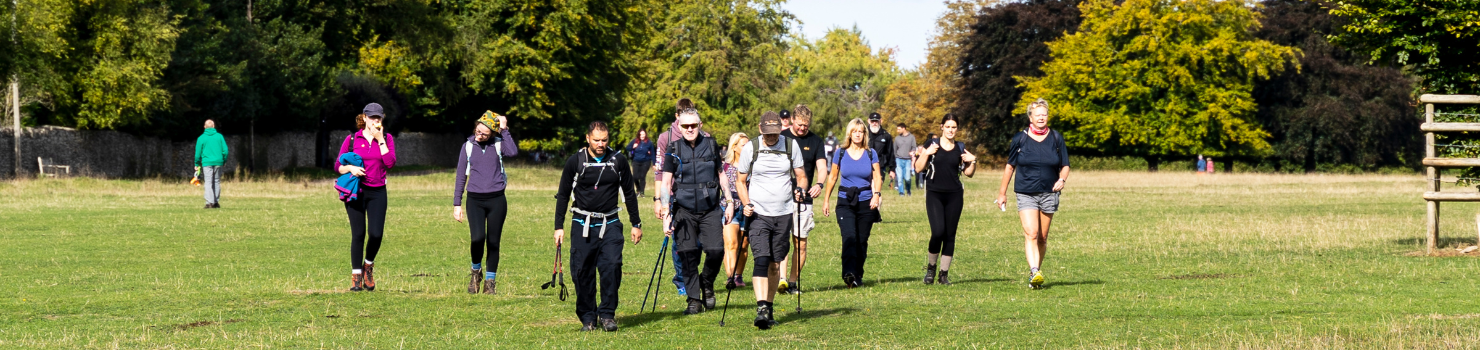 A group of adults walking through a green field, wearing walking gear.