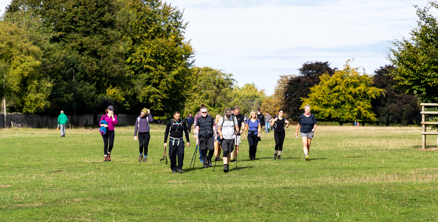 A group of adults walking through a green field, wearing walking gear.