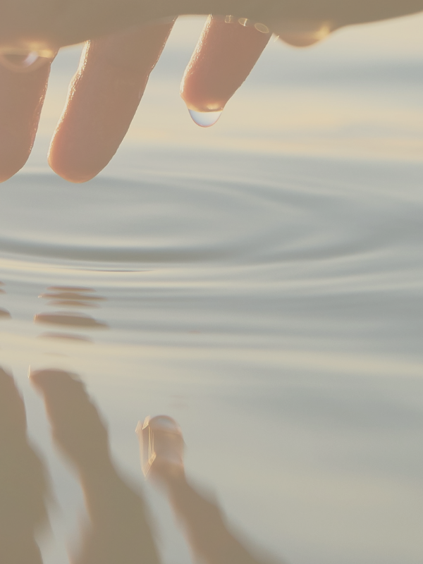 Fingertips gently touching the water creating a ripple effect