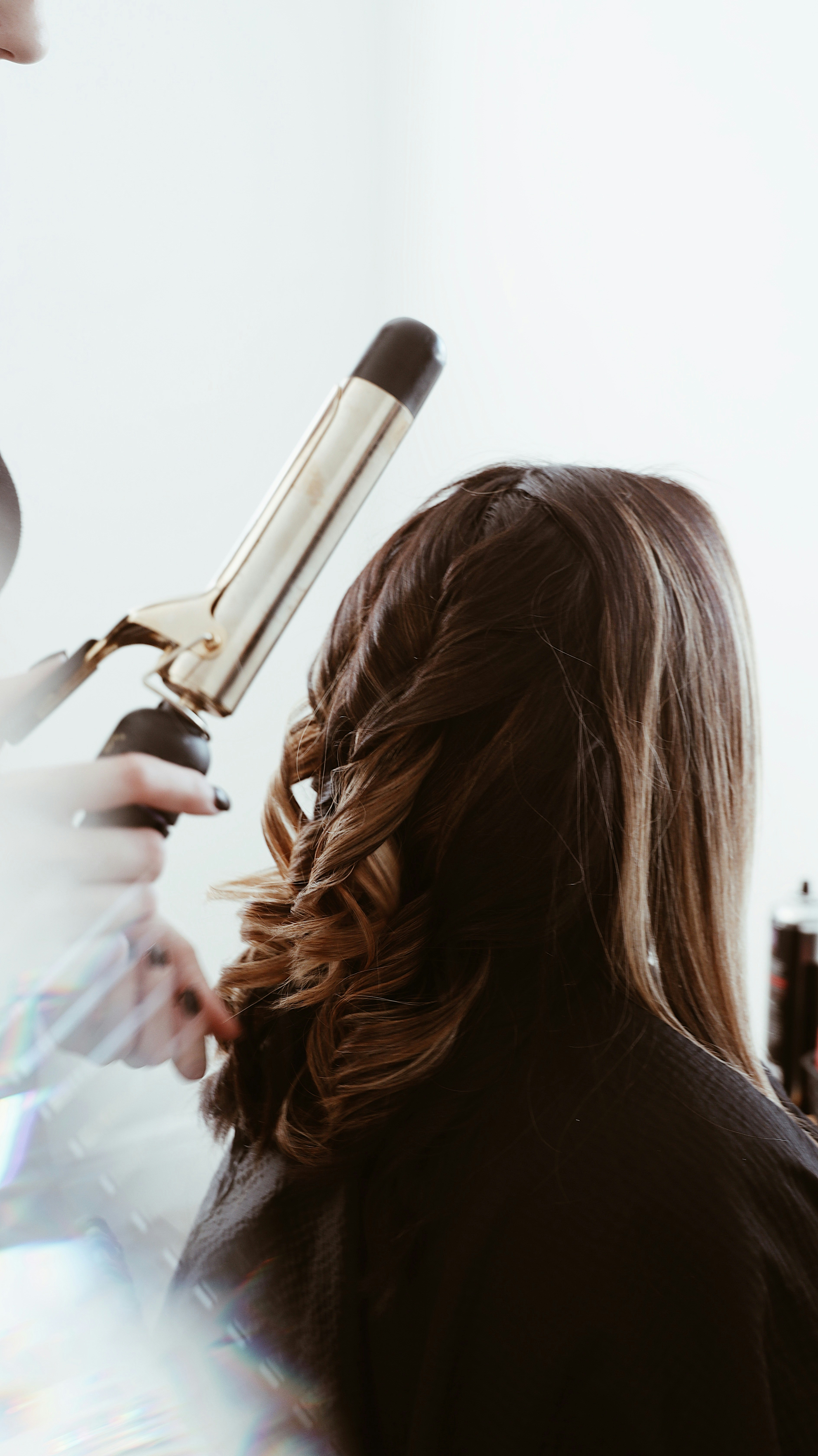 A woman with long hair having her hair curled by a hair stylist