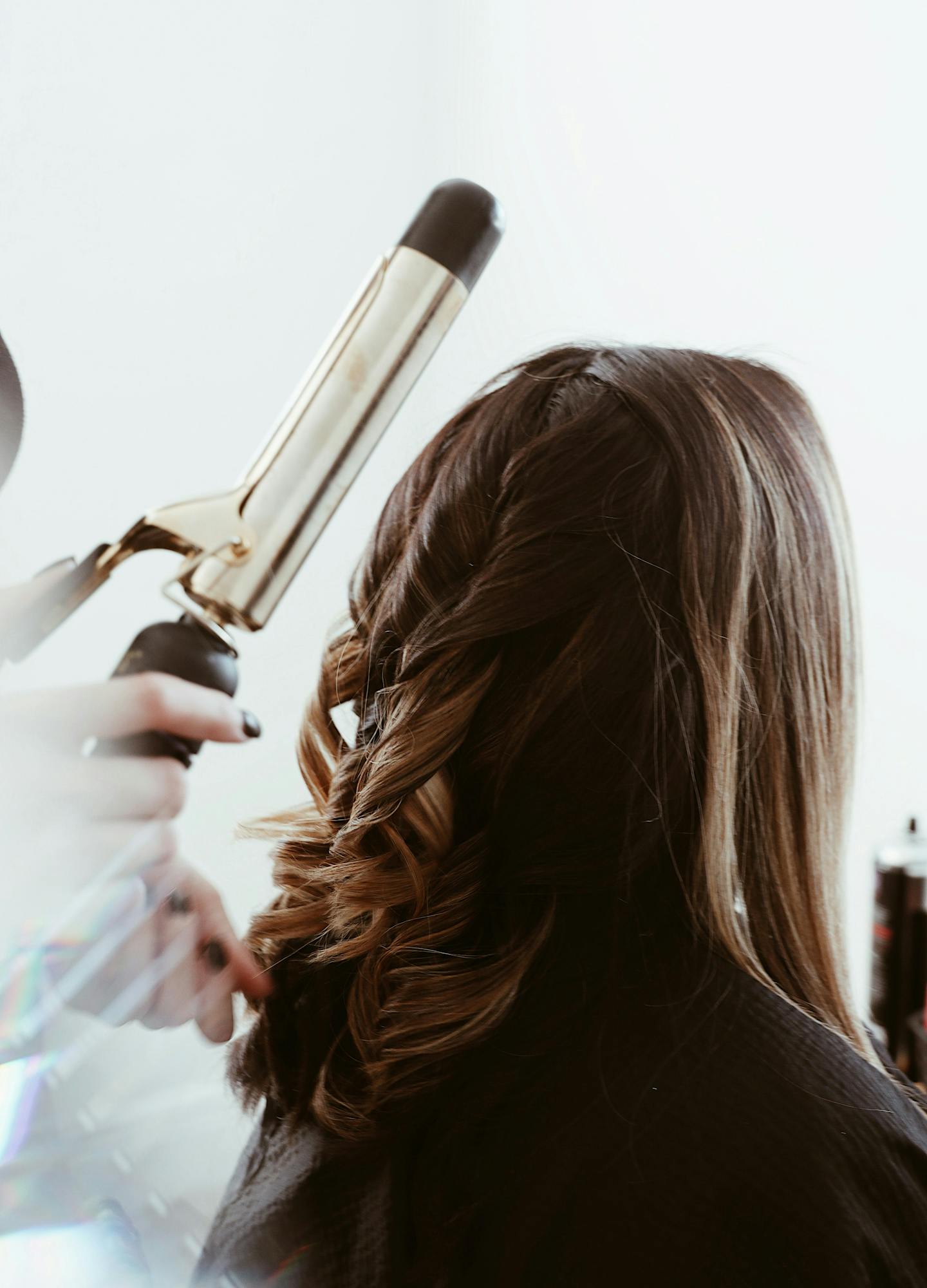 A woman with long hair having her hair curled by a hair stylist