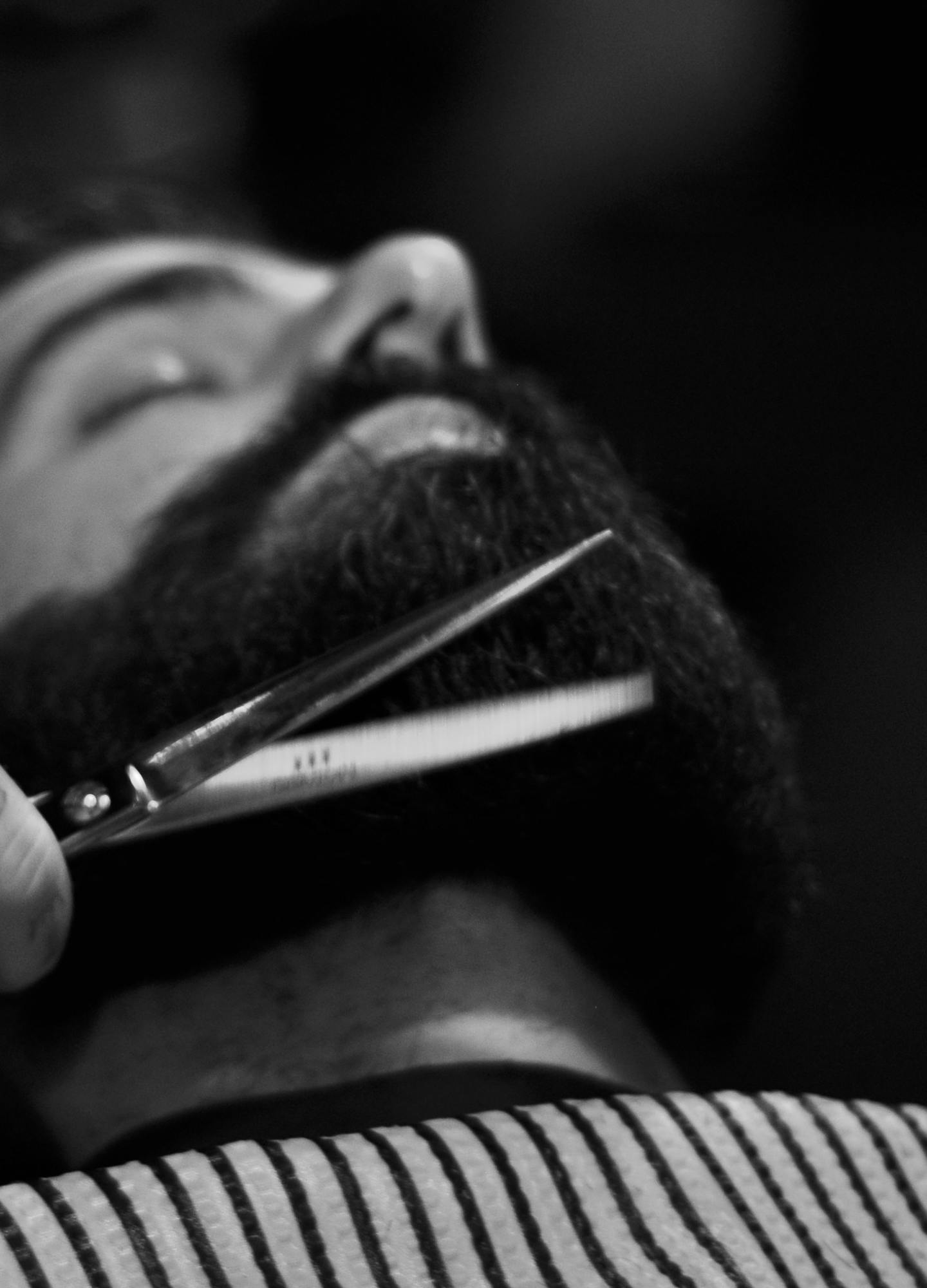 A man in a barbers chair having his beard shaped by a barber