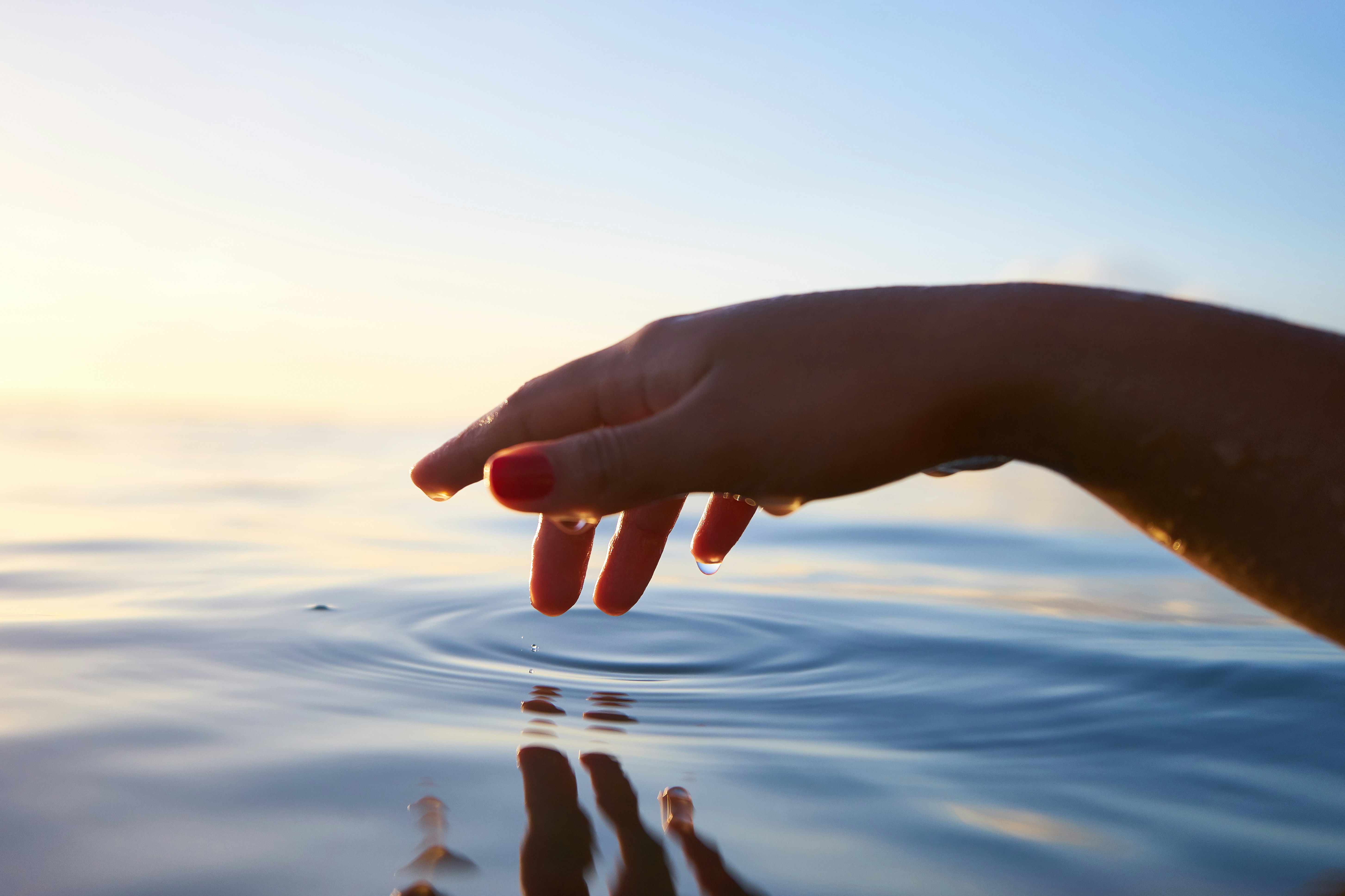 Hand gently touching the water, creating a ripple effect