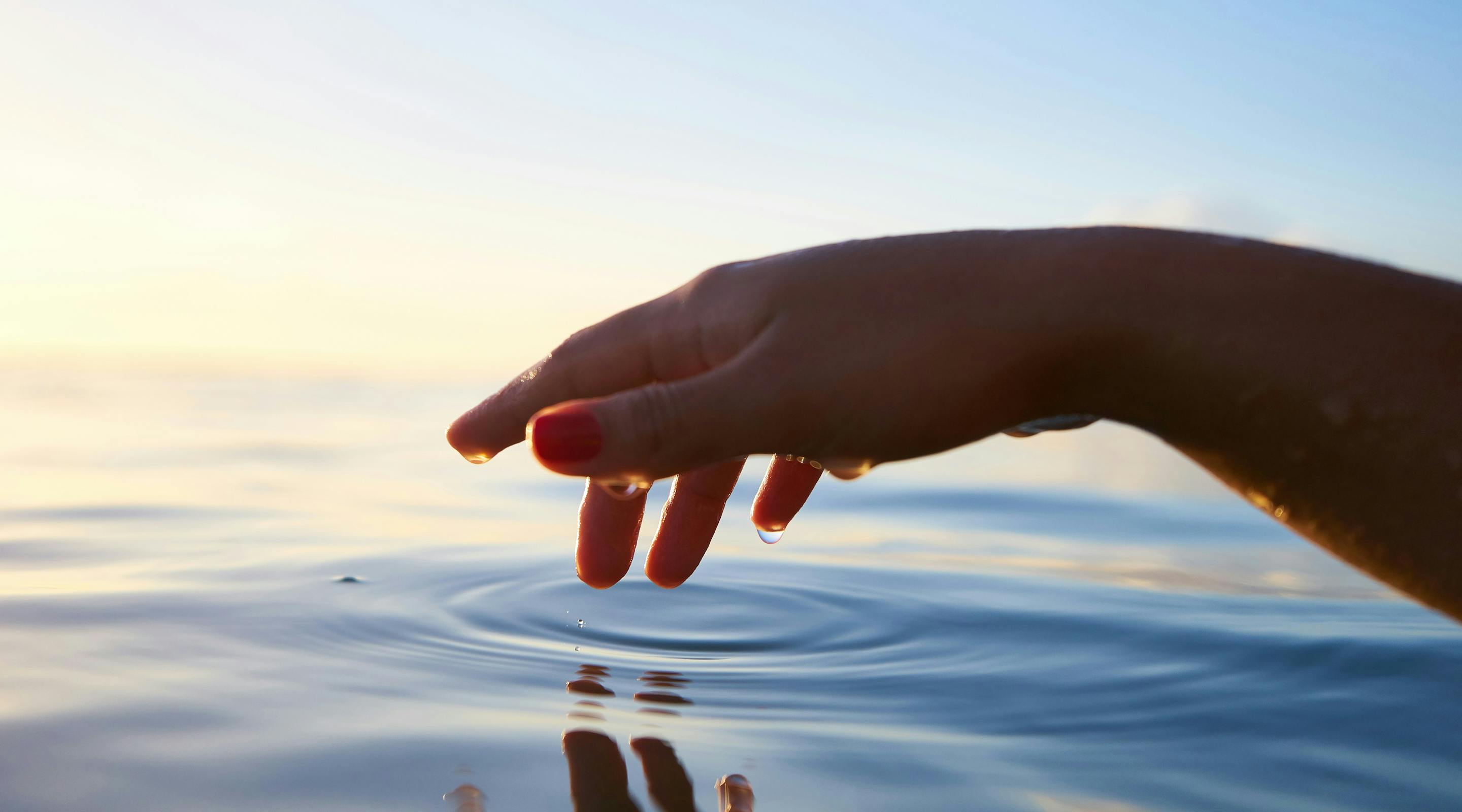 Hand gently touching the water, creating a ripple effect