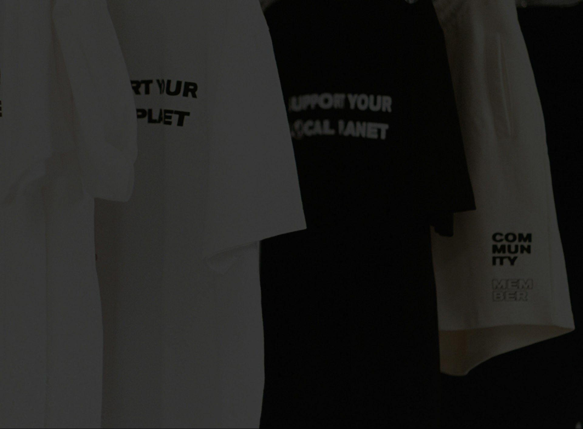 T-shirts in black and white hanging on rack reading Support Your Local Planet Community Member, custom merchandise by MerchCamp