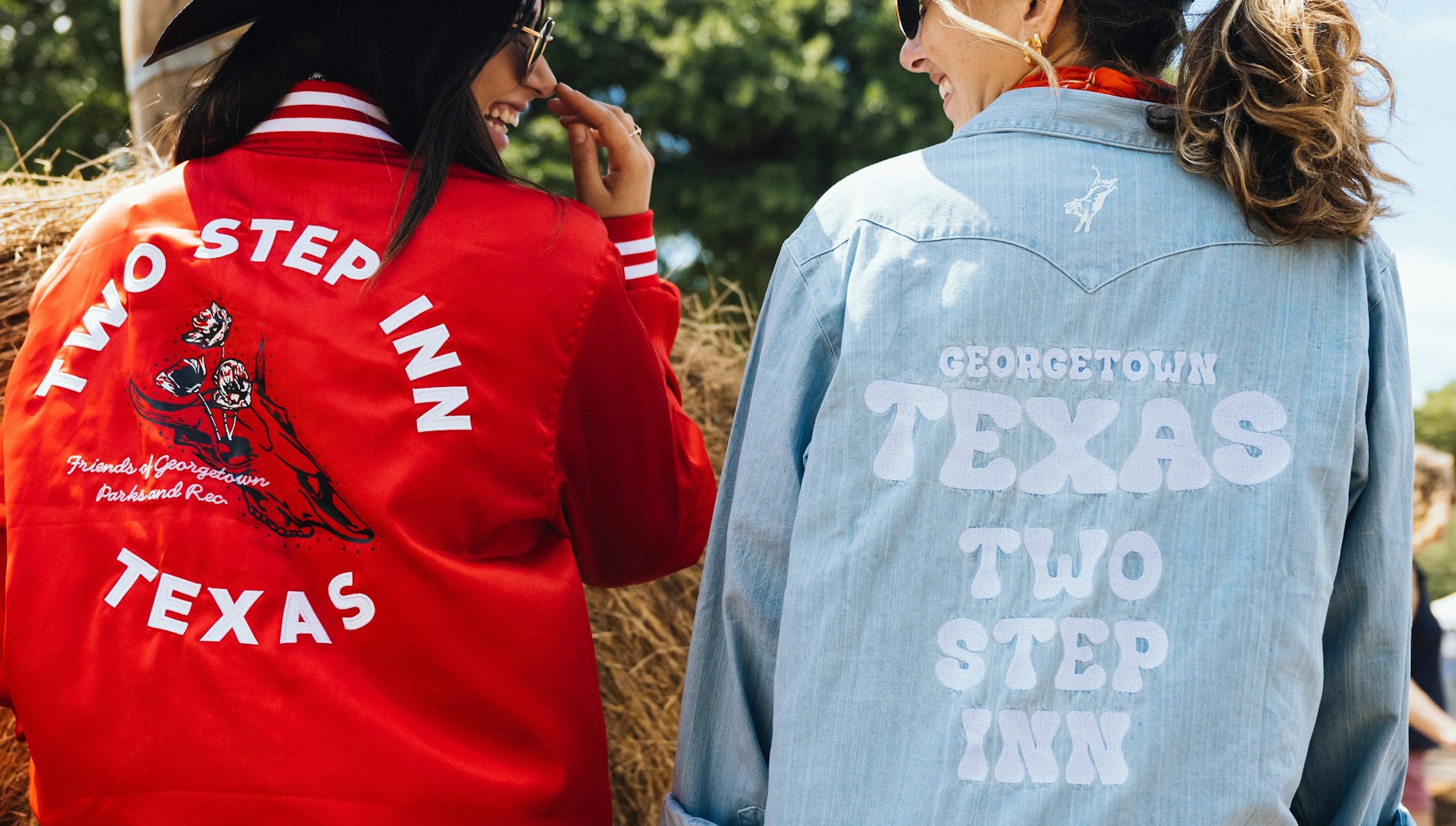 Two women wearing Two Step Inn Texas jackets in red and denim outdoors — MerchCamp custom merchandise