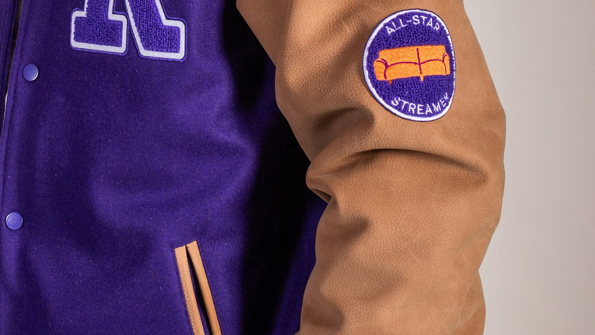 Purple and tan varsity letterman jacket with "All-Star Streamer" couch patch on leather sleeve — MerchCamp custom merchandise