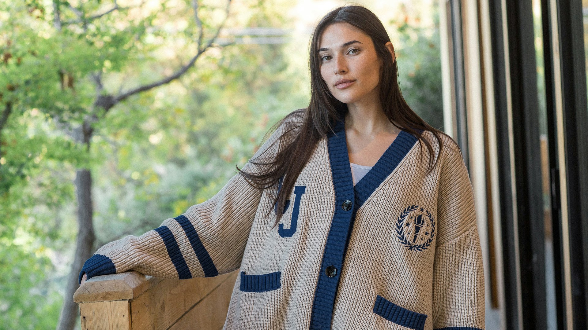 Woman modeling oversized beige and navy varsity-style knit cardigan with embroidered crest detail — MerchCamp custom merchandise