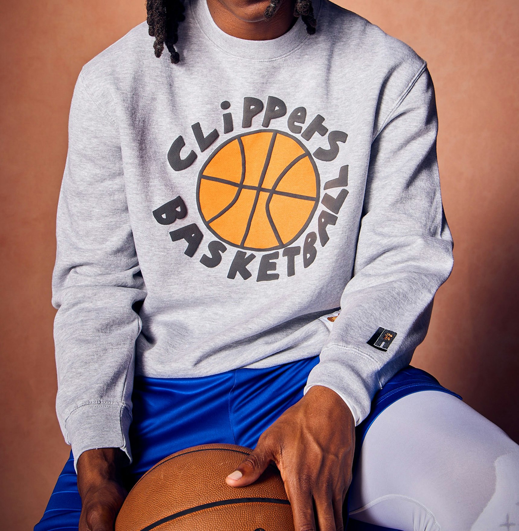 Person in grey Clippers Basketball crewneck sweatshirt holding basketball, wearing blue shorts — LA Clippers merchandise by MerchCamp