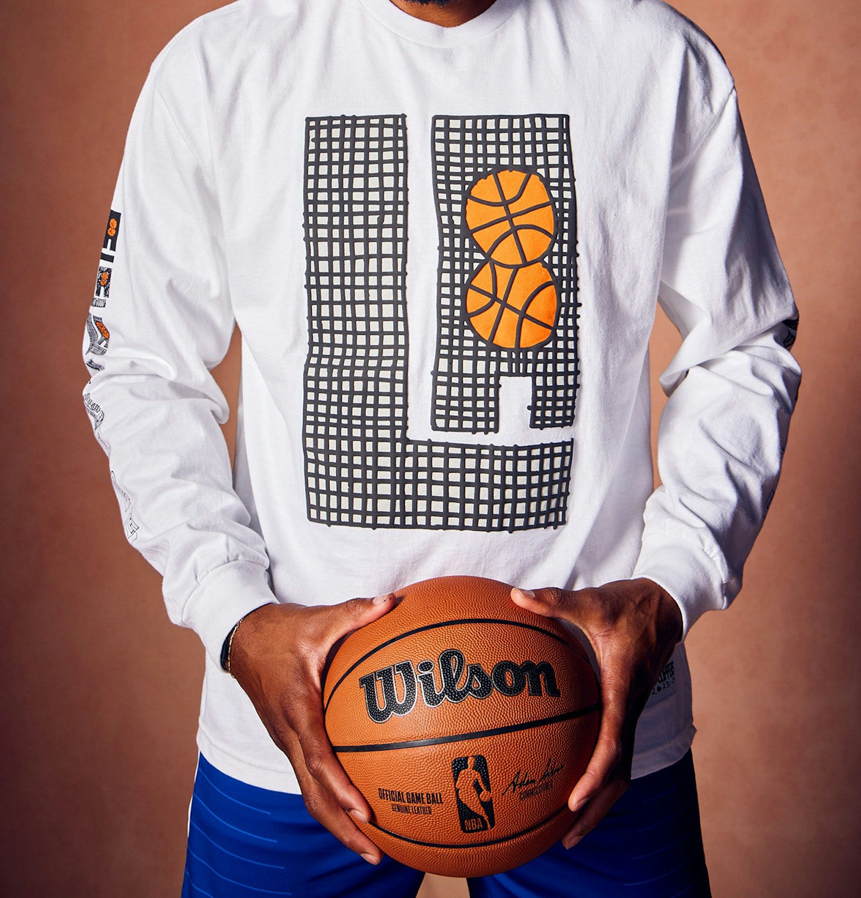 Person wearing white LA Clippers long-sleeve tee holding Wilson NBA official game basketball — LA Clippers merchandise by MerchCamp
