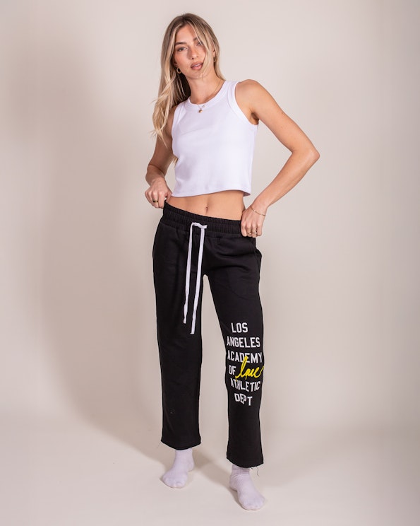 Custom black raw-edge fleece sweatpants with white and yellow screen printed text graphic, produced by MerchCamp for Ruben Rojas