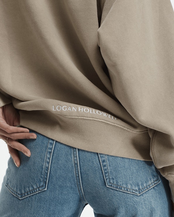 Embroidered tan fleece crewneck sweatshirt with white serif logo at hem, produced by MerchCamp for Logan Hollowell
