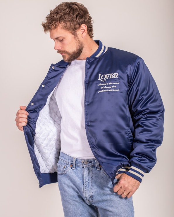 Embroidered navy satin bomber jacket with quilted lining and striped ribbed cuffs, produced by MerchCamp for Ruben Rojas