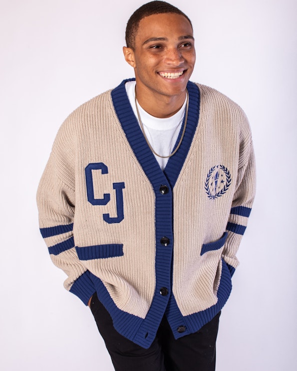 Full custom beige ribbed knit cardigan with navy trim, varsity letter patch, and crest embroidery, produced by MerchCamp for Audiochuck