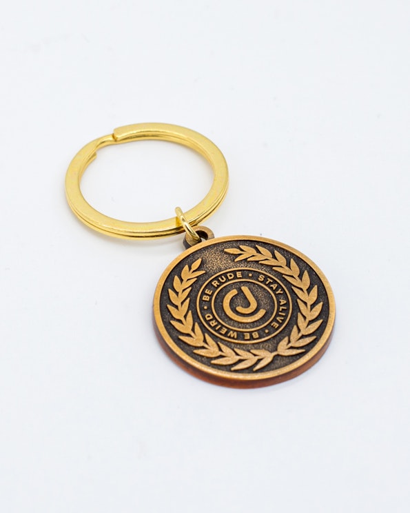 Full custom brushed gold medallion keychain with laurel wreath and embossed crest, produced by MerchCamp for Audiochuck