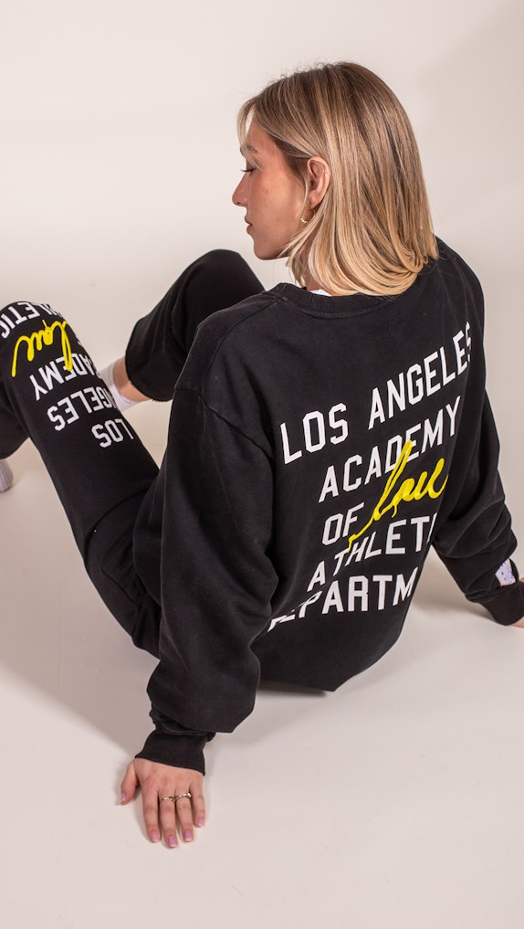 Woman modeling black oversized sweatshirt with Los Angeles Academy Athletic Department graphic print, custom merchandise by MerchCamp