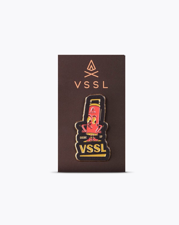 Full custom enamel lapel pin with retro cartoon flask character in red and gold, produced by MerchCamp for VSSL Gear