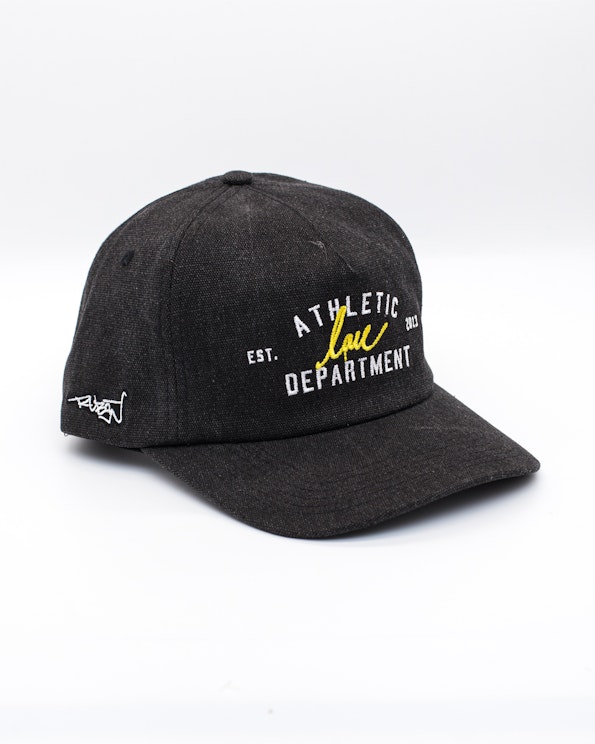 Embroidered charcoal canvas snapback hat with yellow script and white athletic text, produced by MerchCamp for Ruben Rojas