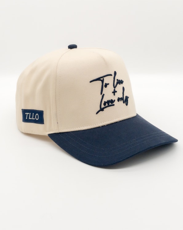 Embroidered cream and navy two-tone snapback with cursive script and woven side label, produced by MerchCamp