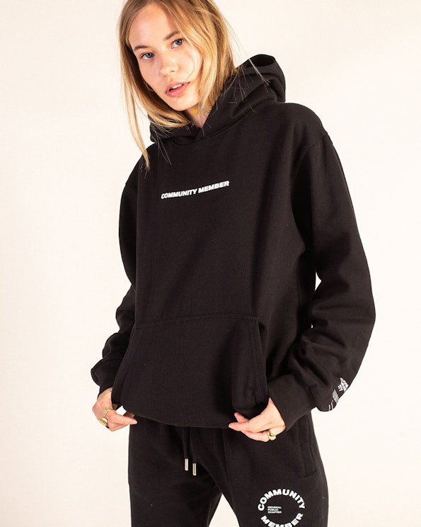 Screen printed black fleece pullover hoodie with white italic "Community Member" text, produced by MerchCamp for Community Member