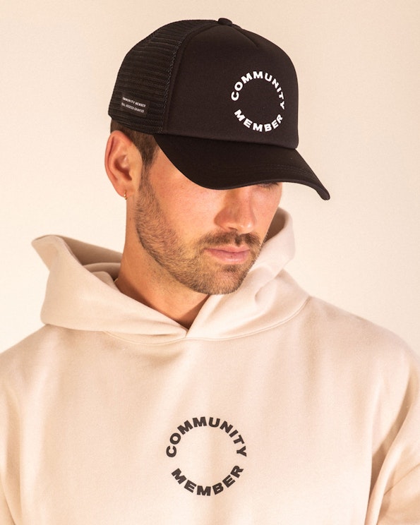 Full custom black foam trucker hat with white circular text logo and mesh back, produced by MerchCamp for Community Member