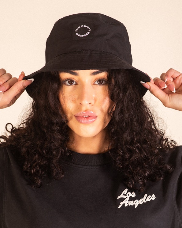 Embroidered black cotton bucket hat with white circular "Community Member" logo, produced by MerchCamp for Community Member