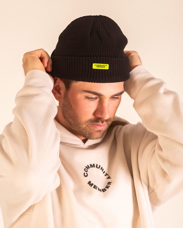 Full custom black ribbed knit beanie with neon yellow woven brand label, produced by MerchCamp for Community Member