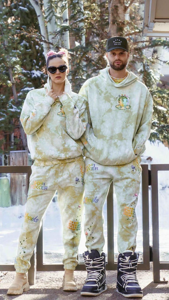 Two people wearing matching green tie-dye Sofi Tukker hoodies and sweatpants in snowy outdoor setting — MerchCamp custom merchandise