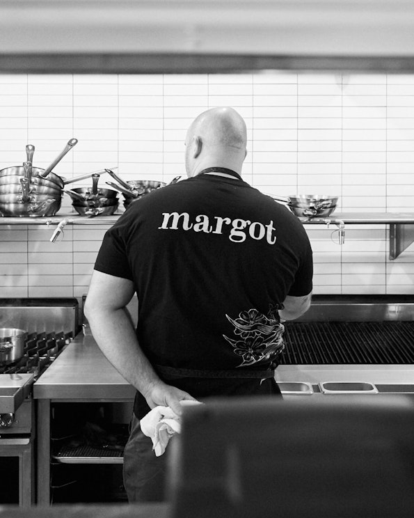 Screen printed black cotton staff tee with white serif logo and floral graphic, produced by MerchCamp for Margot