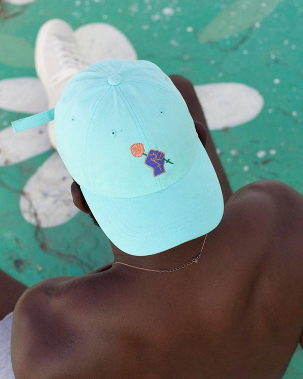 Embroidered mint cotton dad hat with raised fist holding rose motif, produced by MerchCamp for Bloom & Plume