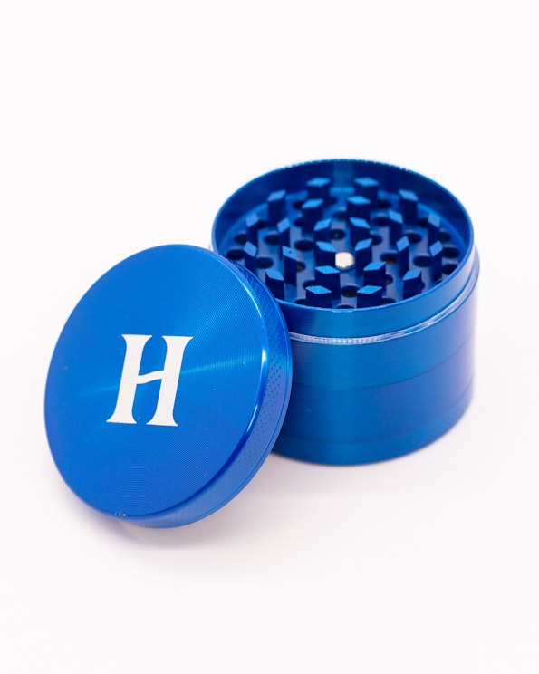 Custom blue anodized aluminum herb grinder with white H logo on lid, produced by MerchCamp for Herb