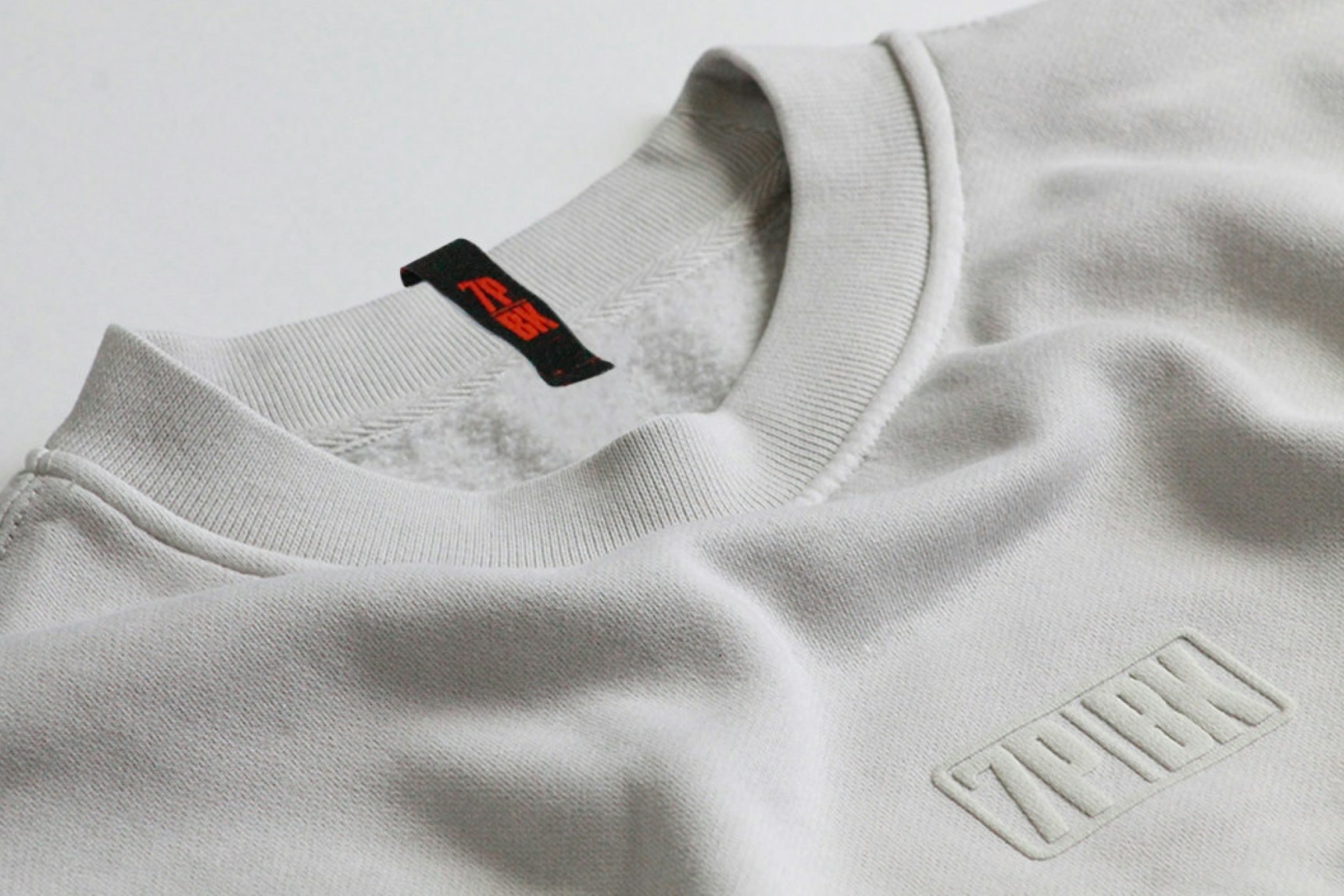 Close-up of light gray crewneck sweatshirt with tonal embossed logo and black — WAVE Sports + Entertainment merchandise by MerchCamp