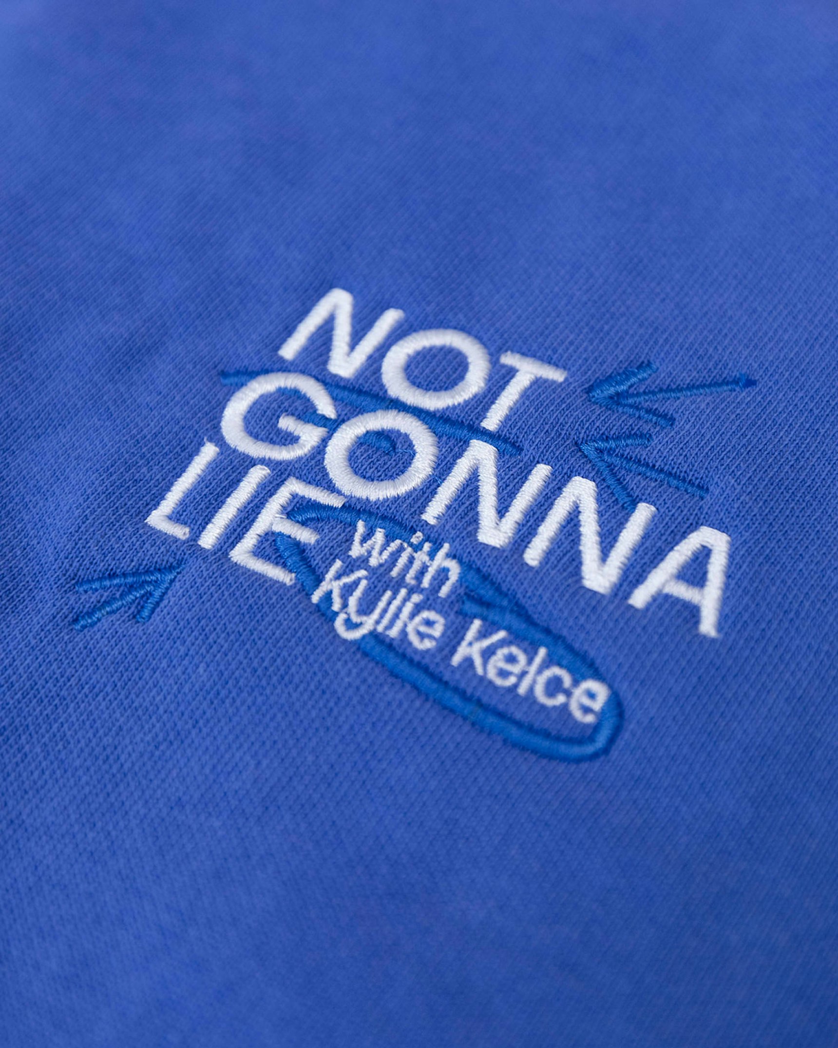 Close-up of white embroidered "Not Gonna Lie with Kylie Kelce" logo on royal — WAVE Sports + Entertainment merchandise by MerchCamp