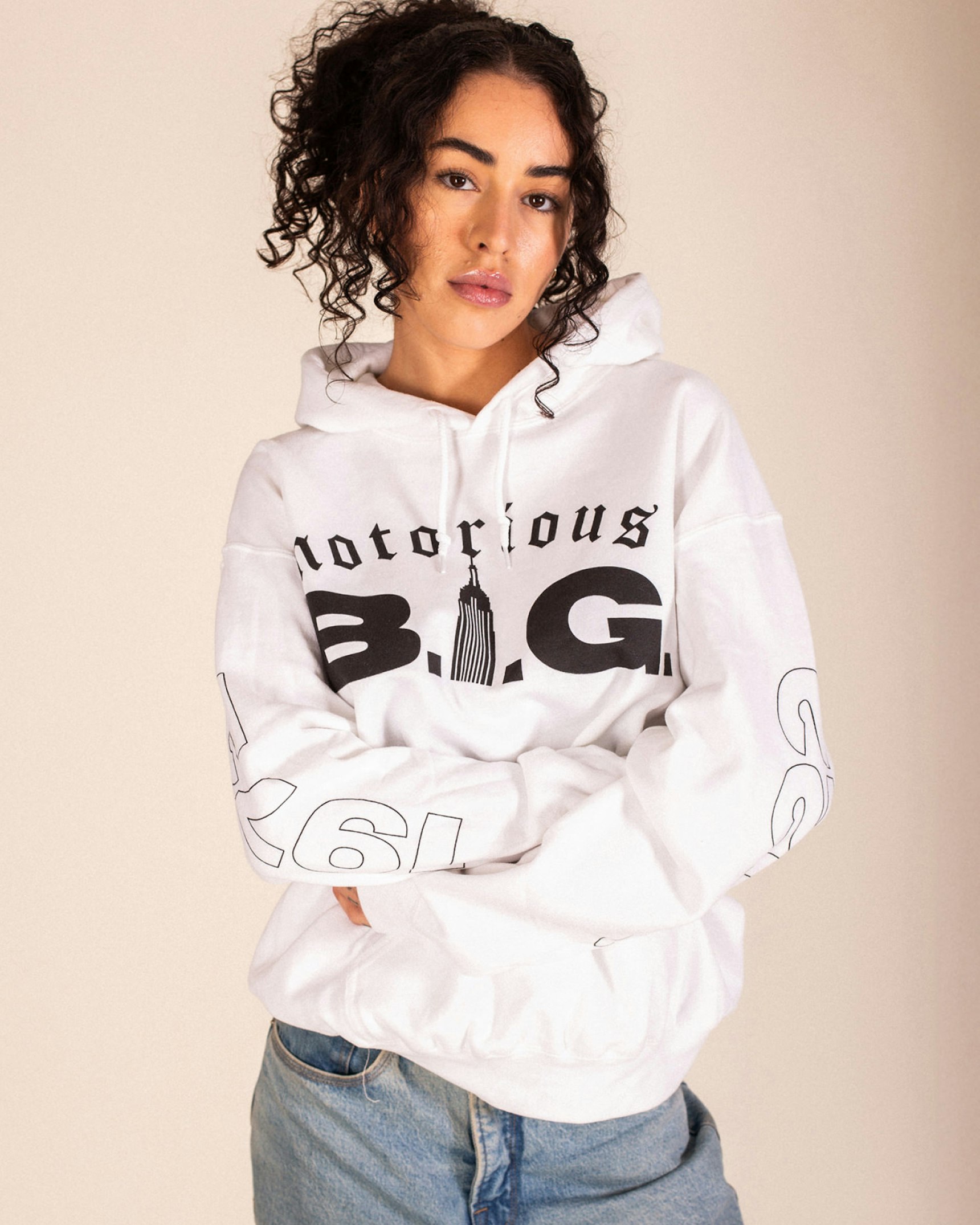 Woman in white Notorious B.I.G. hoodie with Empire State Building graphic and light jeans — Biggie Smalls merchandise by MerchCamp
