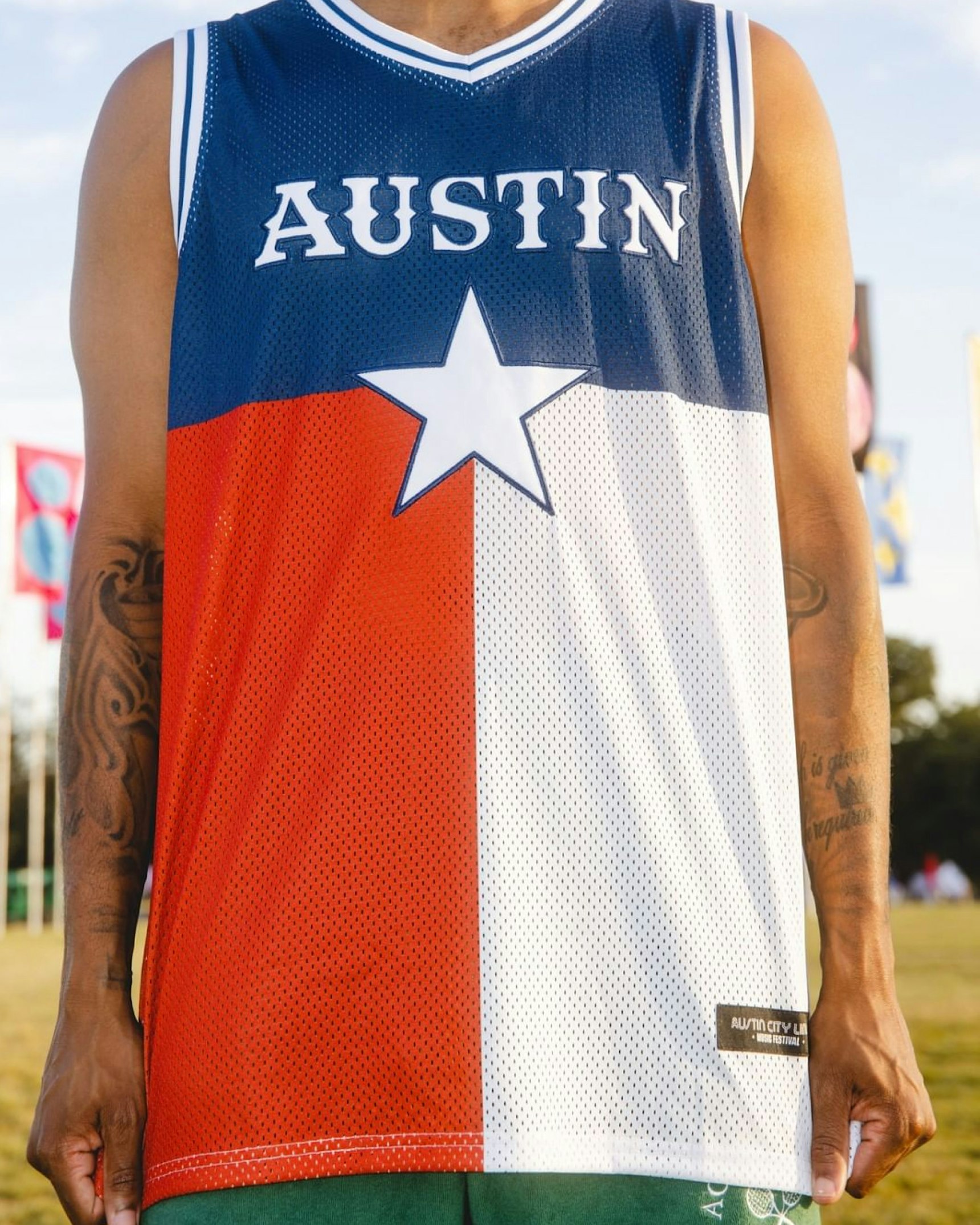 Person wearing Austin Texas flag basketball jersey at Austin City Limits music festival outdoors — Live Nation merchandise by MerchCamp