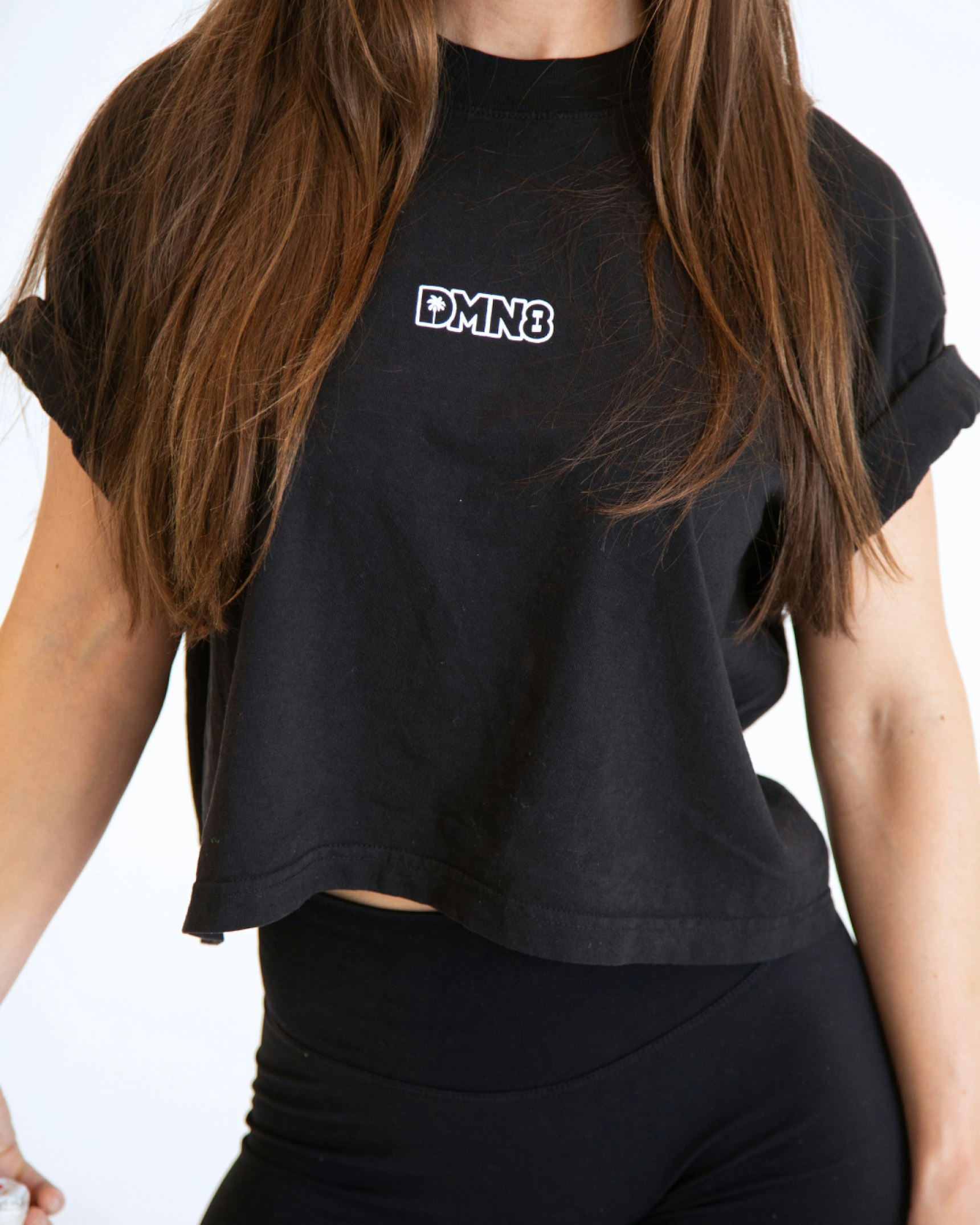 Woman wearing black DMN8 branded crop top with rolled sleeves and black leggings — DMN8 merchandise by MerchCamp