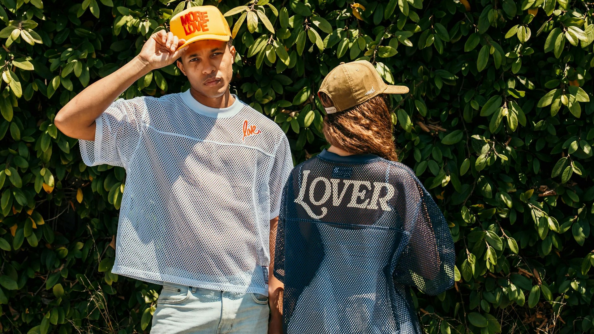 Two models in mesh jerseys and caps posing outdoors against lush green foliage — Ruben Rojas merchandise by MerchCamp