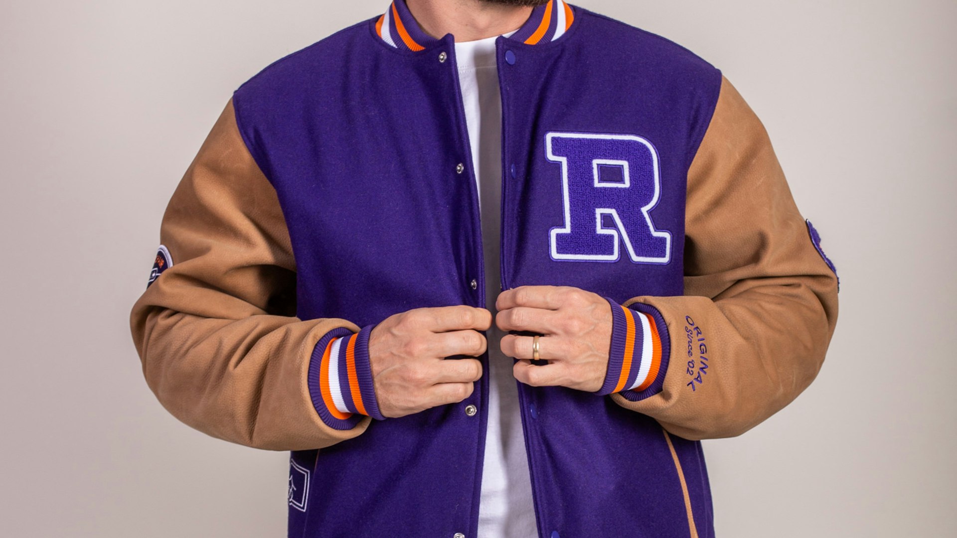 Close-up of man wearing purple varsity letterman jacket with chenille R patch and tan leather sleeves — Roku merchandise by MerchCamp