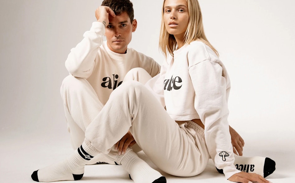 Man and woman modeling matching cream Alice Mushrooms branded sweatshirts and joggers in studio, produced by MerchCamp for Alice Mushrooms