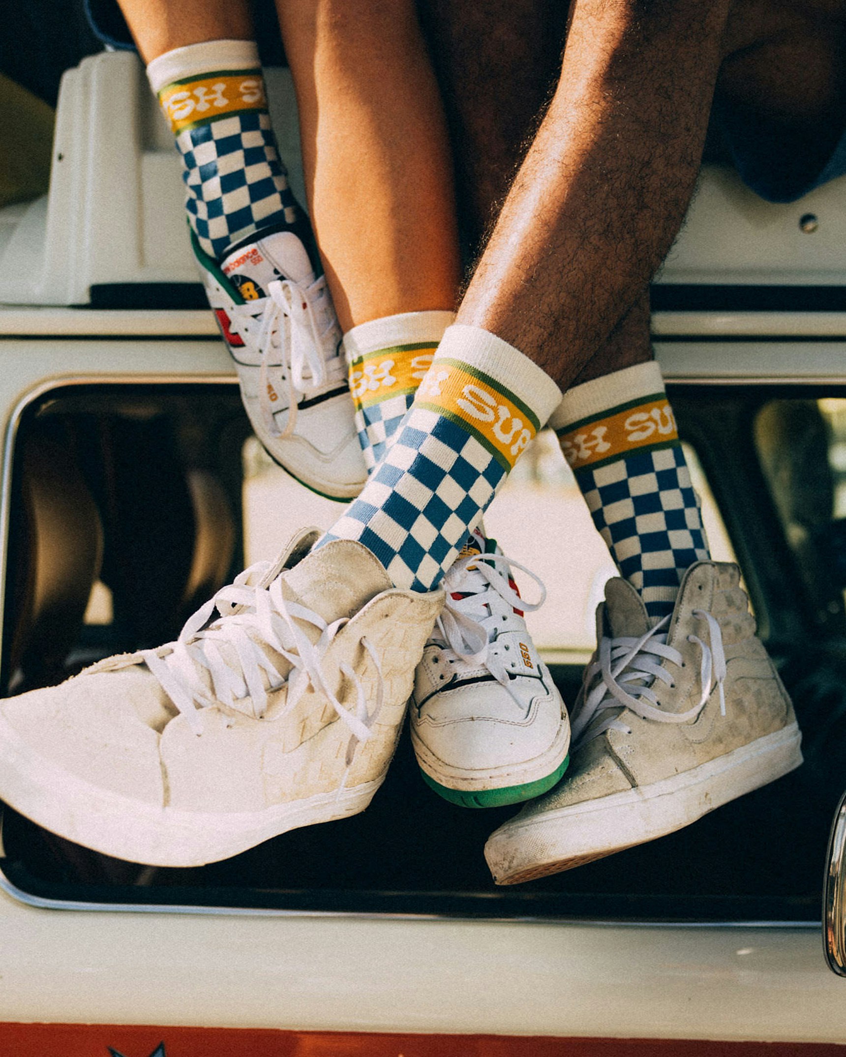 Two pairs of legs wearing Supermush checkered blue-and-white socks with white sneakers dangling — Supermush merchandise by MerchCamp