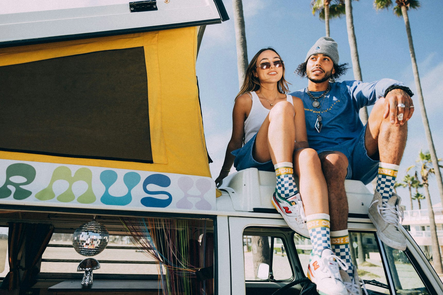 Two models sitting atop a vintage VW van wearing Supermush branded socks and casual beachwear — Supermush merchandise by MerchCamp