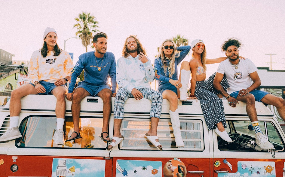 Group of friends sitting on a vintage VW bus wearing custom Supermush branded apparel at sunset, produced by MerchCamp for Supermush