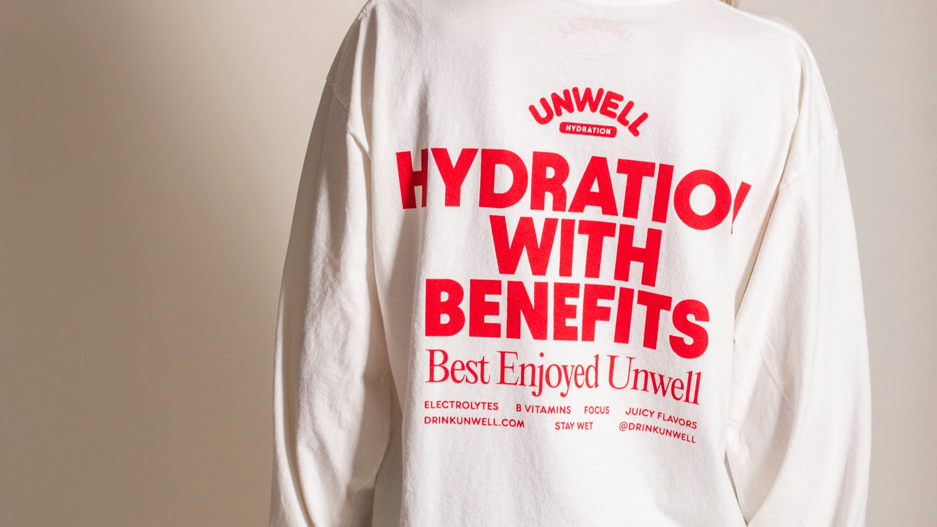Back of white long-sleeve tee with red Unwell Hydration branding and taglines — Unwell merchandise by MerchCamp