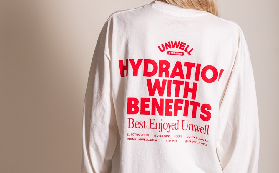 White long-sleeve tee with red screen printed Unwell Hydration branding and tagline on back, produced by MerchCamp for Unwell