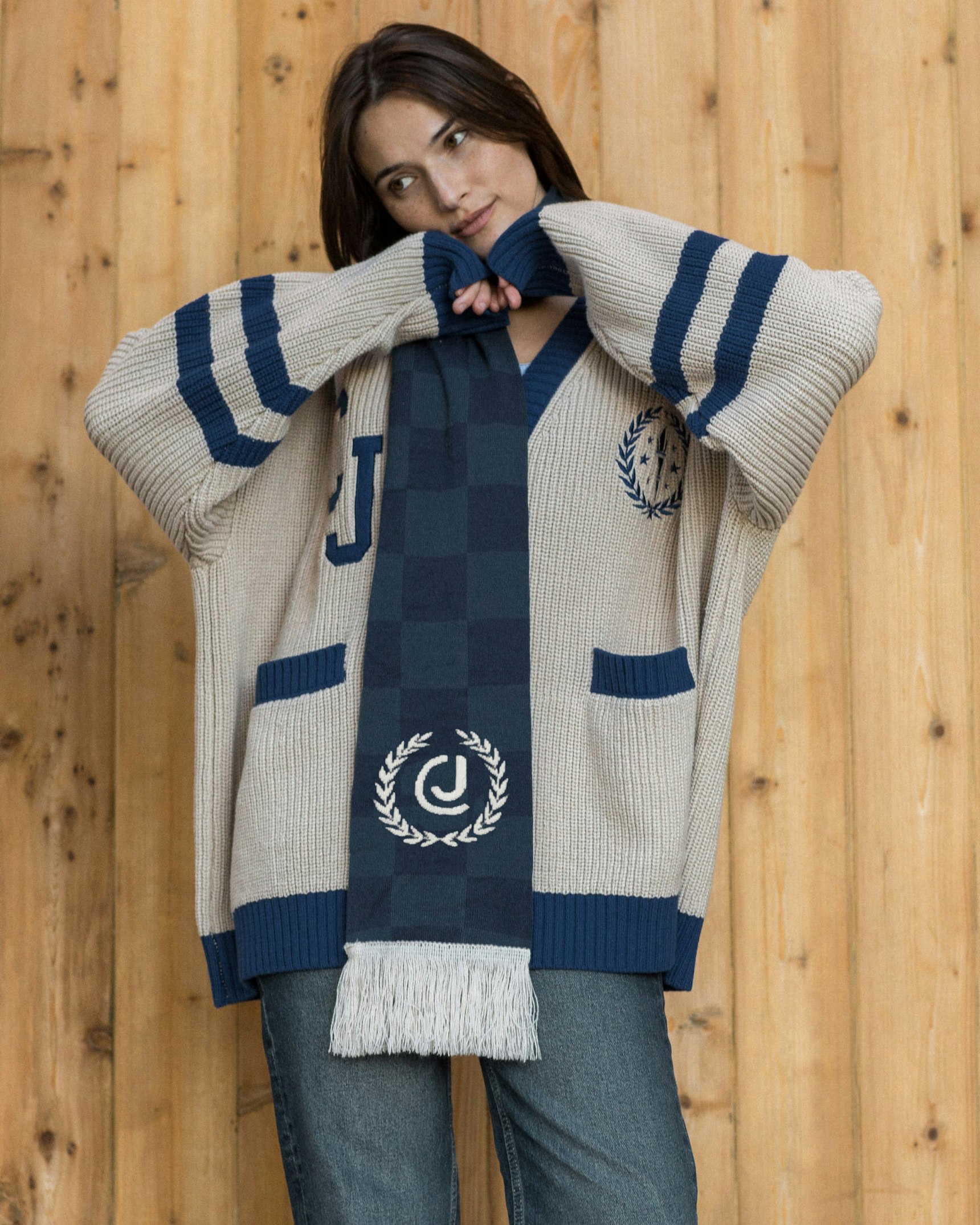 Woman in cream and navy varsity cardigan with checkered scarf featuring CJ laurel crest logo — Crime Junkie merchandise by MerchCamp