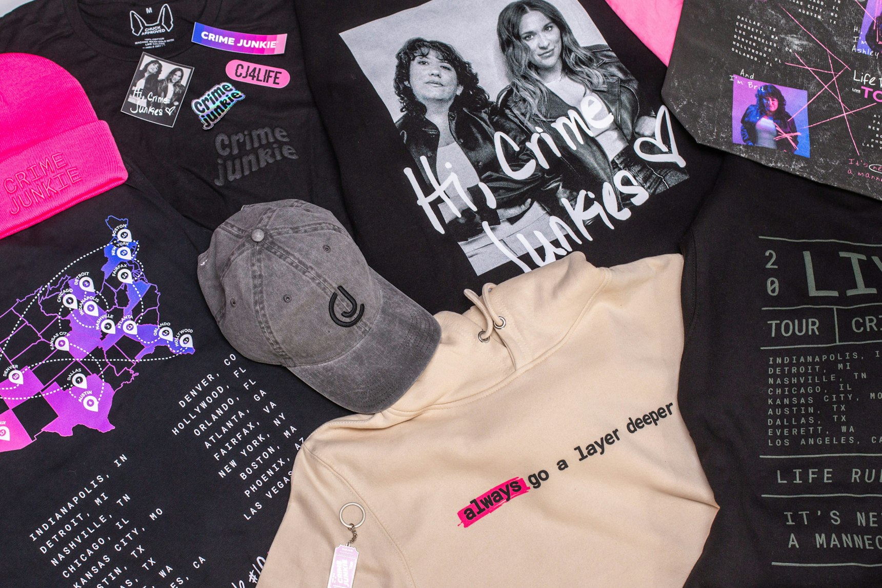 Flat lay of Crime Junkie tour merchandise including hoodies, tees, hats, and stickers on black — Crime Junkie merchandise by MerchCamp